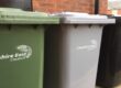 Green, silver and black wheelies bins in a row in front of a wall