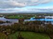 A serene aerial view capturing a flooded countryside with trees and farmlands under a cloudy sky