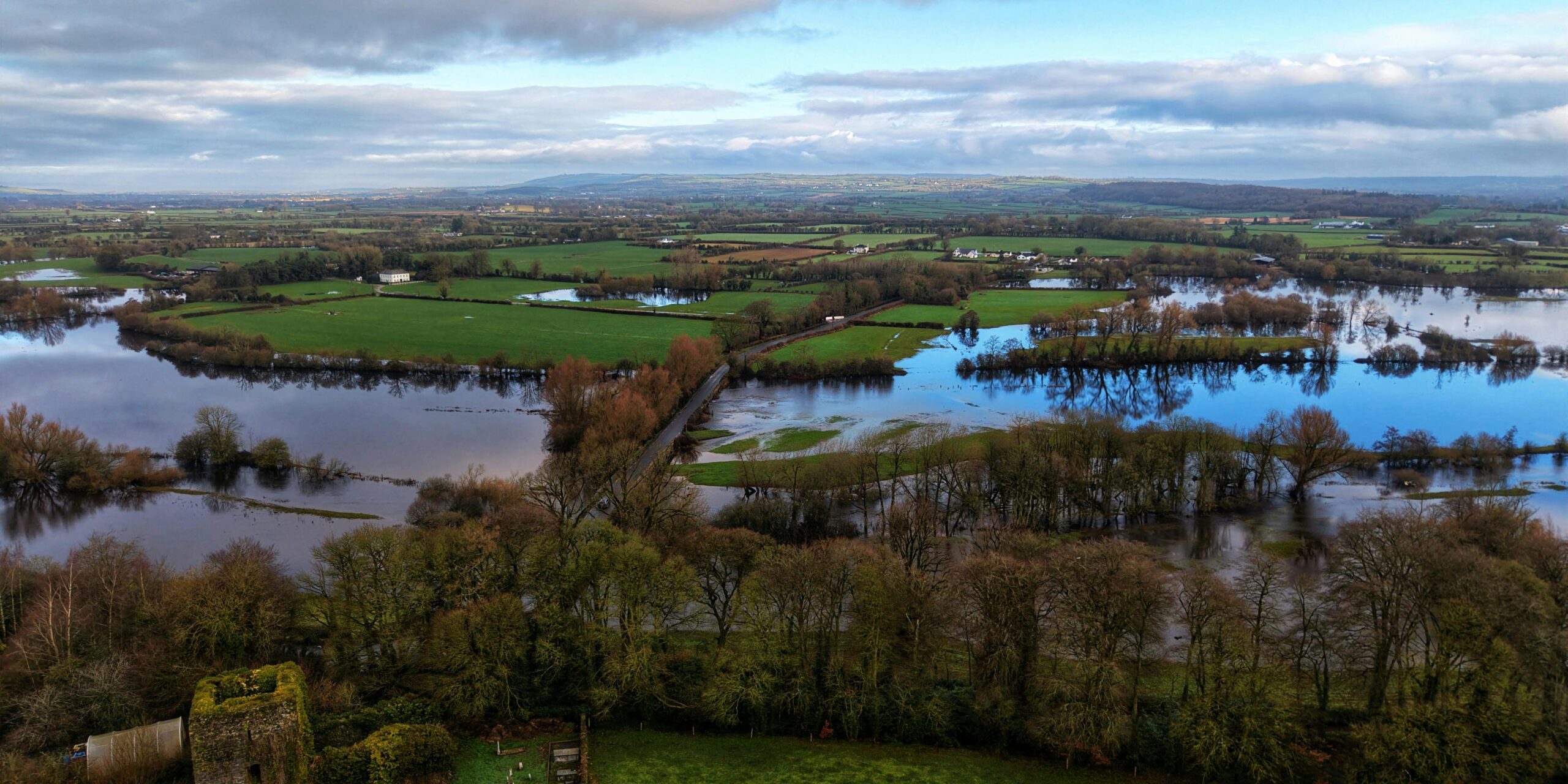 pexels-jaysphotography-36210447 A serene aerial view capturing a flooded countryside with trees and farmlands under a cloudy sky